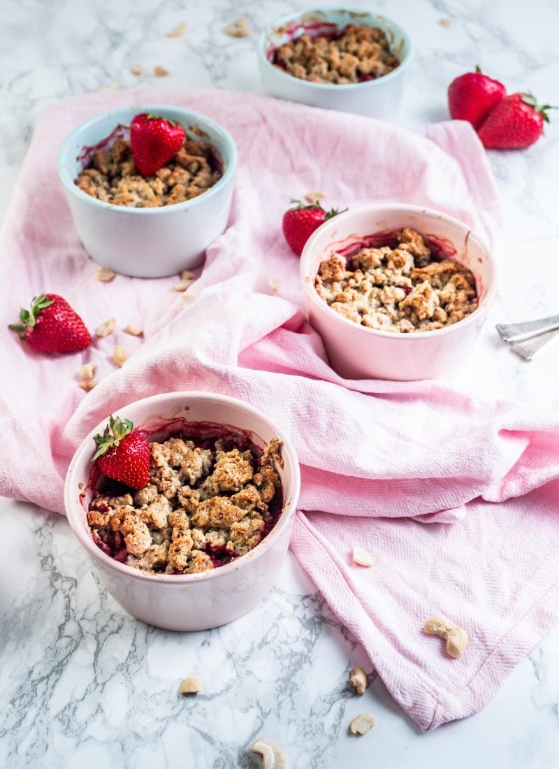 Strawberry Rhubarb Crumble in small ramekins with strawberries and cashews strewn around