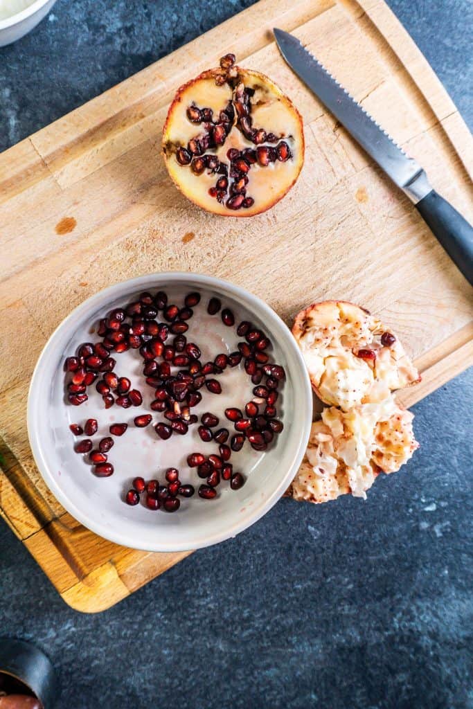 Pomegranate seeds in a bowl, with the flesh of the pomegranate lying next to it