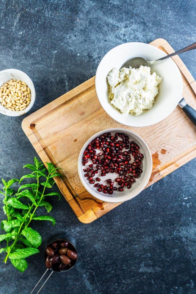 Whipped cottage cheese and feta in a bowl with olives, mint leaves, and pine nuts surrounded in order to prepare a creamy whipped feta dip