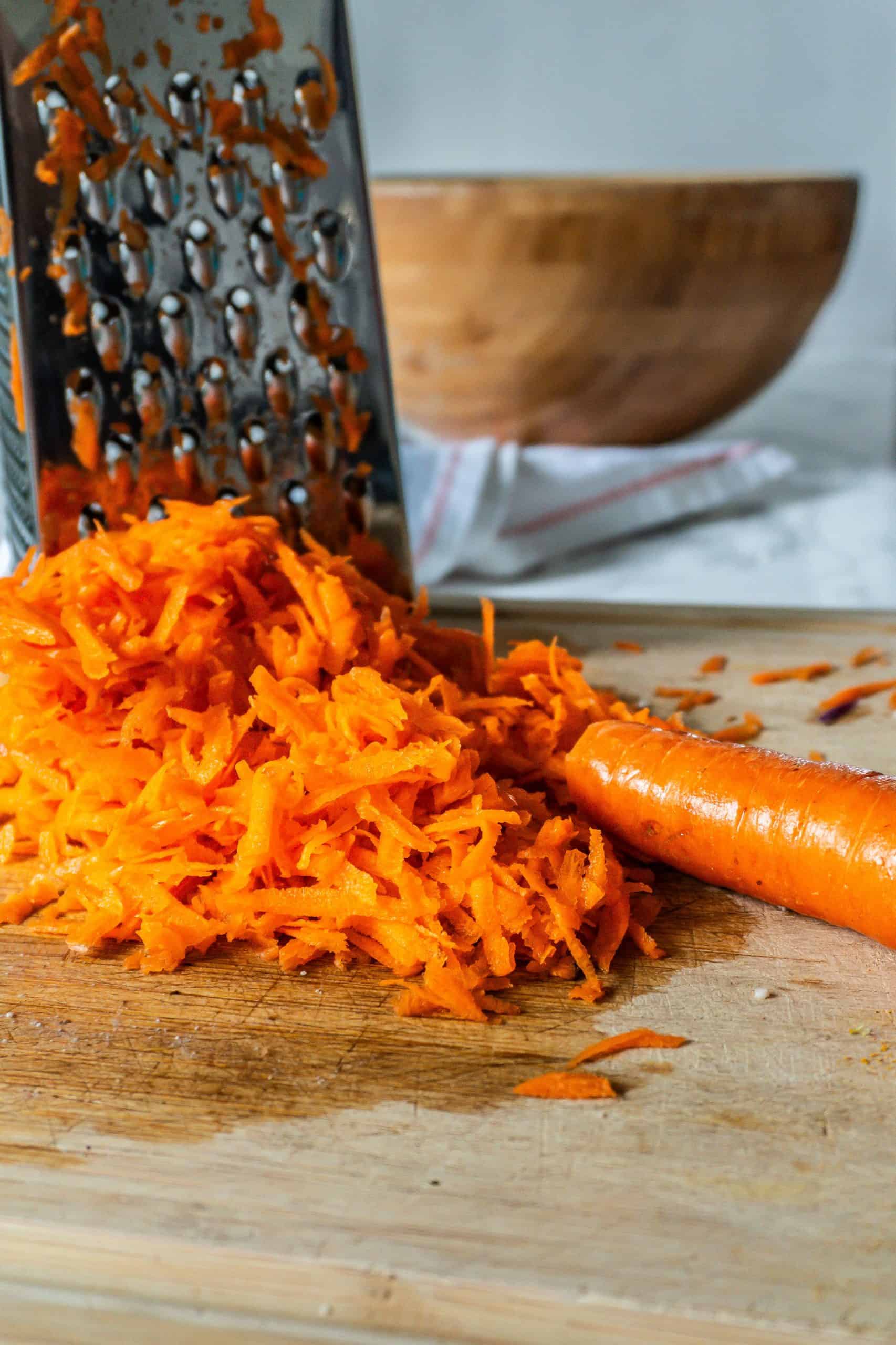 Carrot being grated with a grater in the background