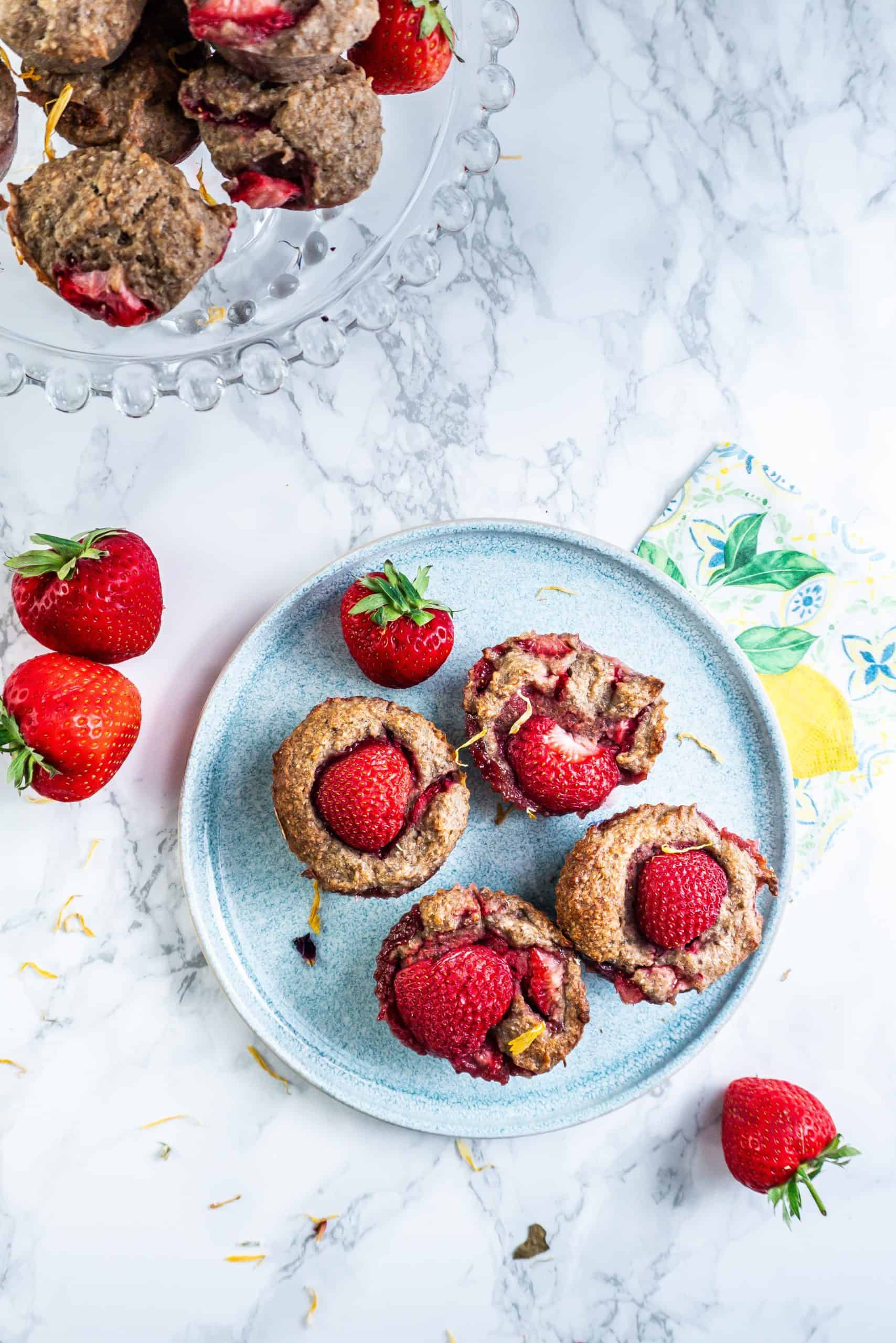 Strawberry Banana Muffins on a plate with some smaller muffins visible on a cake stand in the back; photographed from above