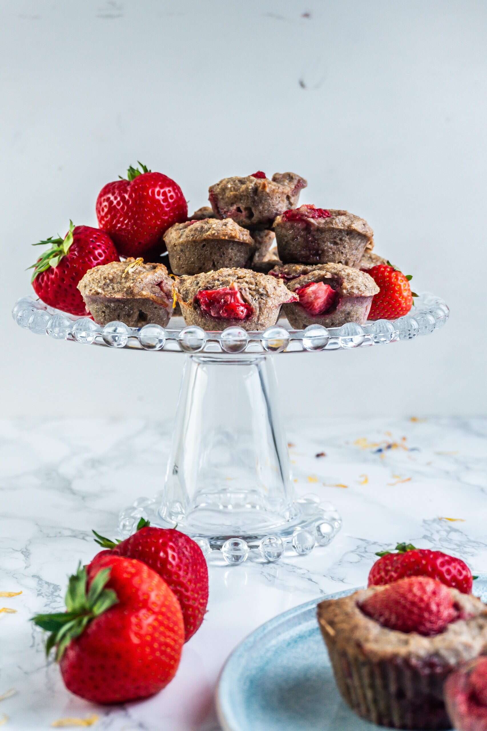 Mini Strawberry Banana Muffins on a small cake stand with some decorated strawberries scattered around