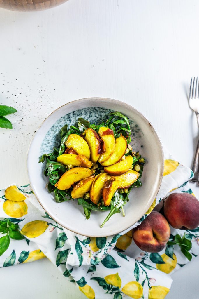 Cherry tomatoes, rocket, basil, and walnuts in a bowl with a balsamic glaze added in a bowl, with grilled courgette and grilled peach added