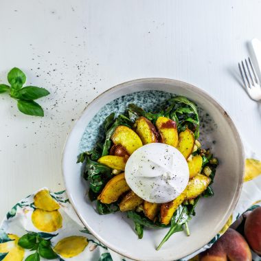 Grilled Peach Salad with Burrata on a plate with a kitchen towel, peaches, and basil visible in the background