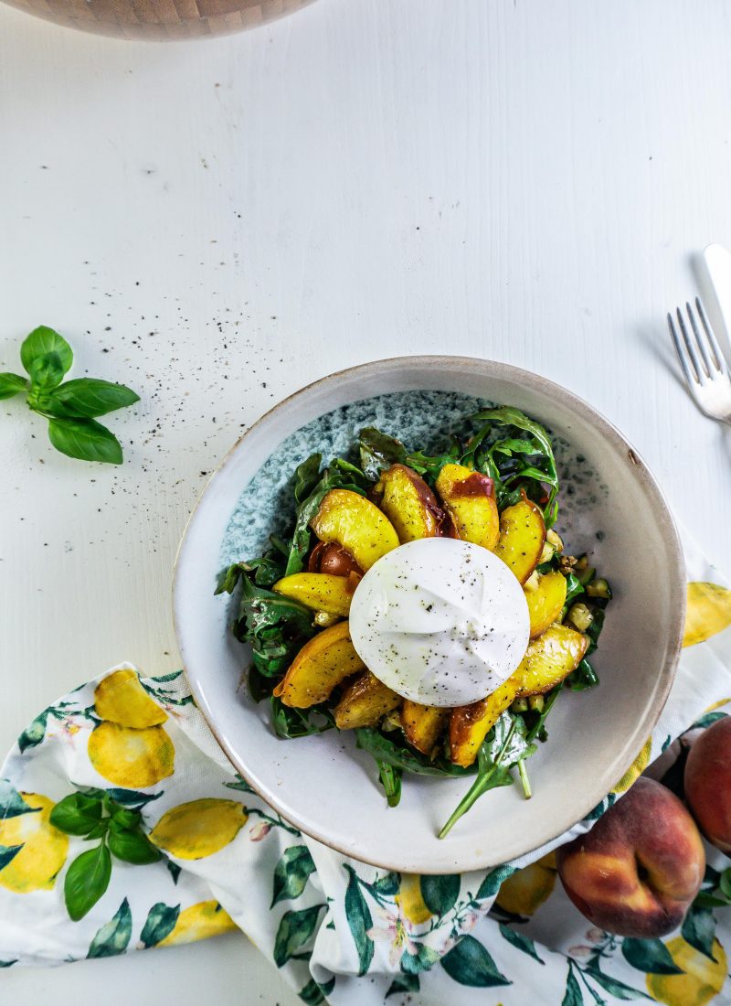 Grilled Peach Salad with Burrata on a plate with a kitchen towel, peaches, and basil visible in the background
