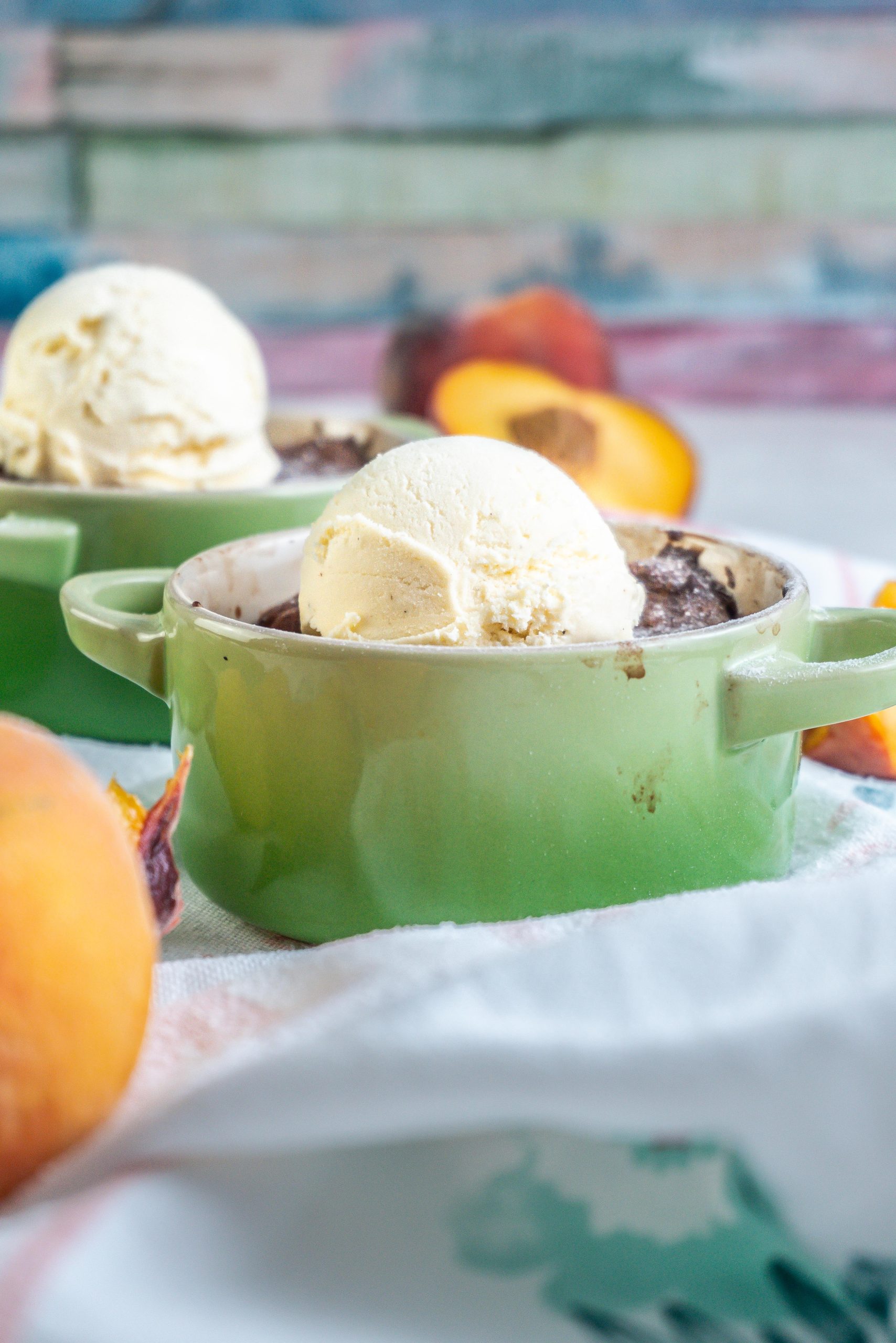 Mini Peach Cobbler in a ramekin dish with some ice cream on top and a second cobbler visible in the background