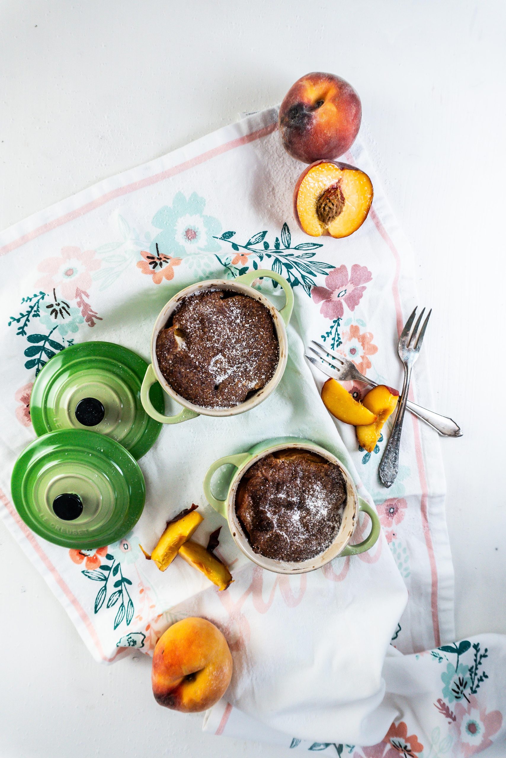 Mini Peach Cobblers in small ramekins with peaches strewn around and two forks lying on the side