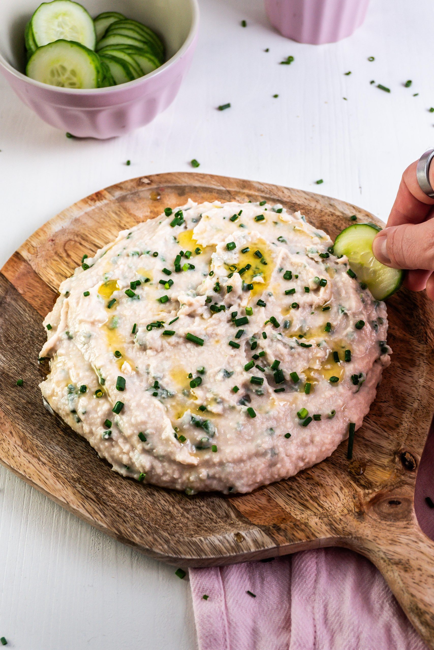 Quick and Easy Butterbean Dip on a wooden plate with a cucumber being dipped into the dip