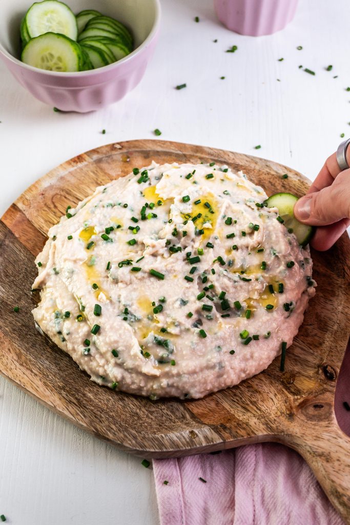 Quick and Easy Butterbean Dip on a wooden plate with a cucumber being dipped into the dip