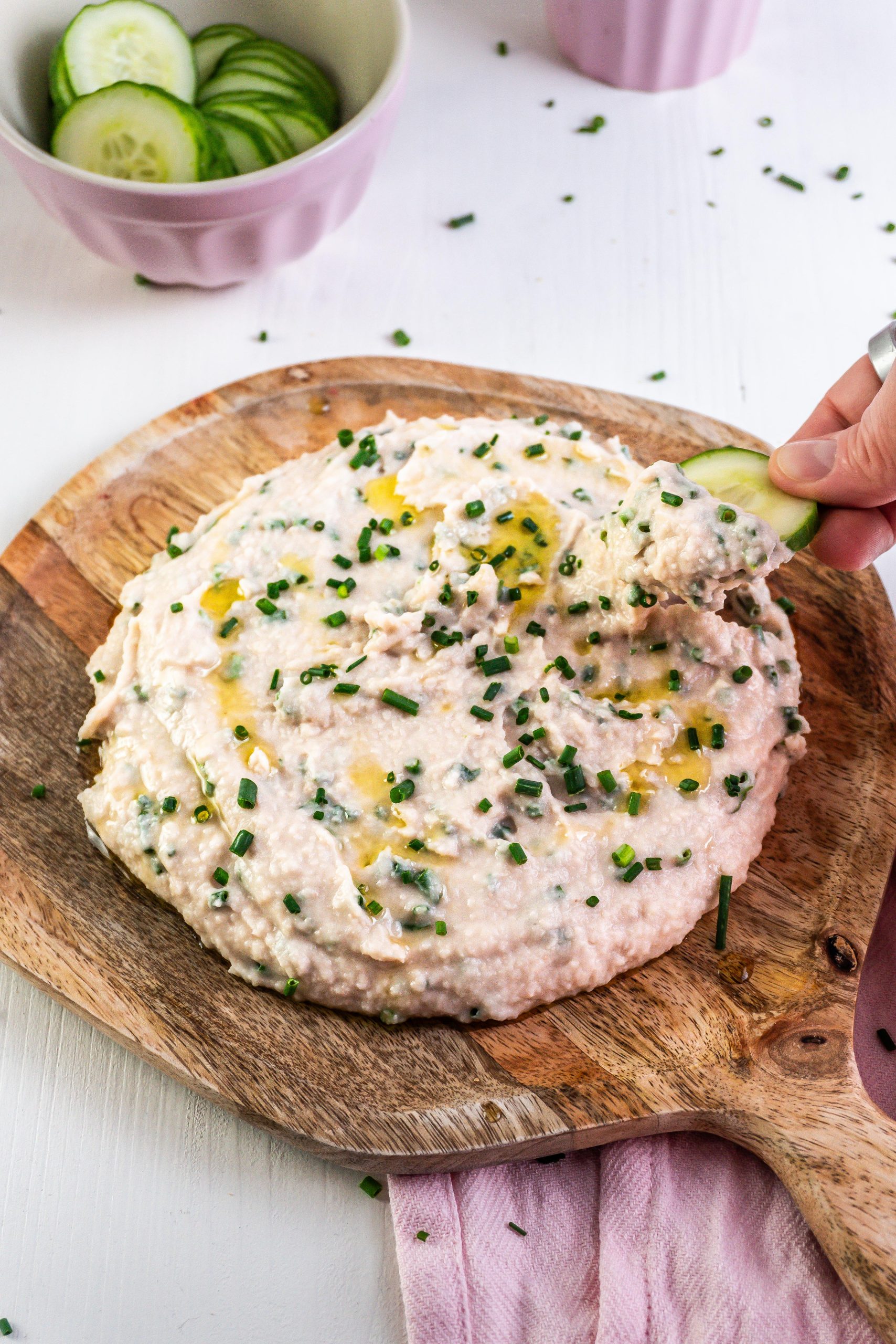 Quick and Easy Butterbean Dip on a wooden plate with a cucumber being dipped into the dip