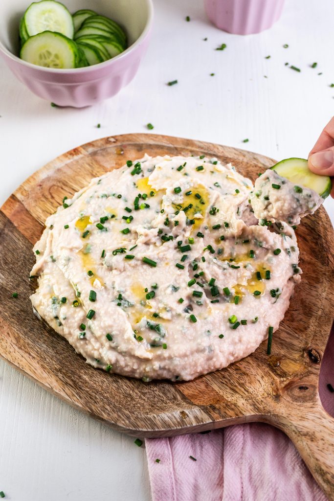 Quick and Easy Butterbean Dip on a wooden plate with a cucumber being dipped into the dip
