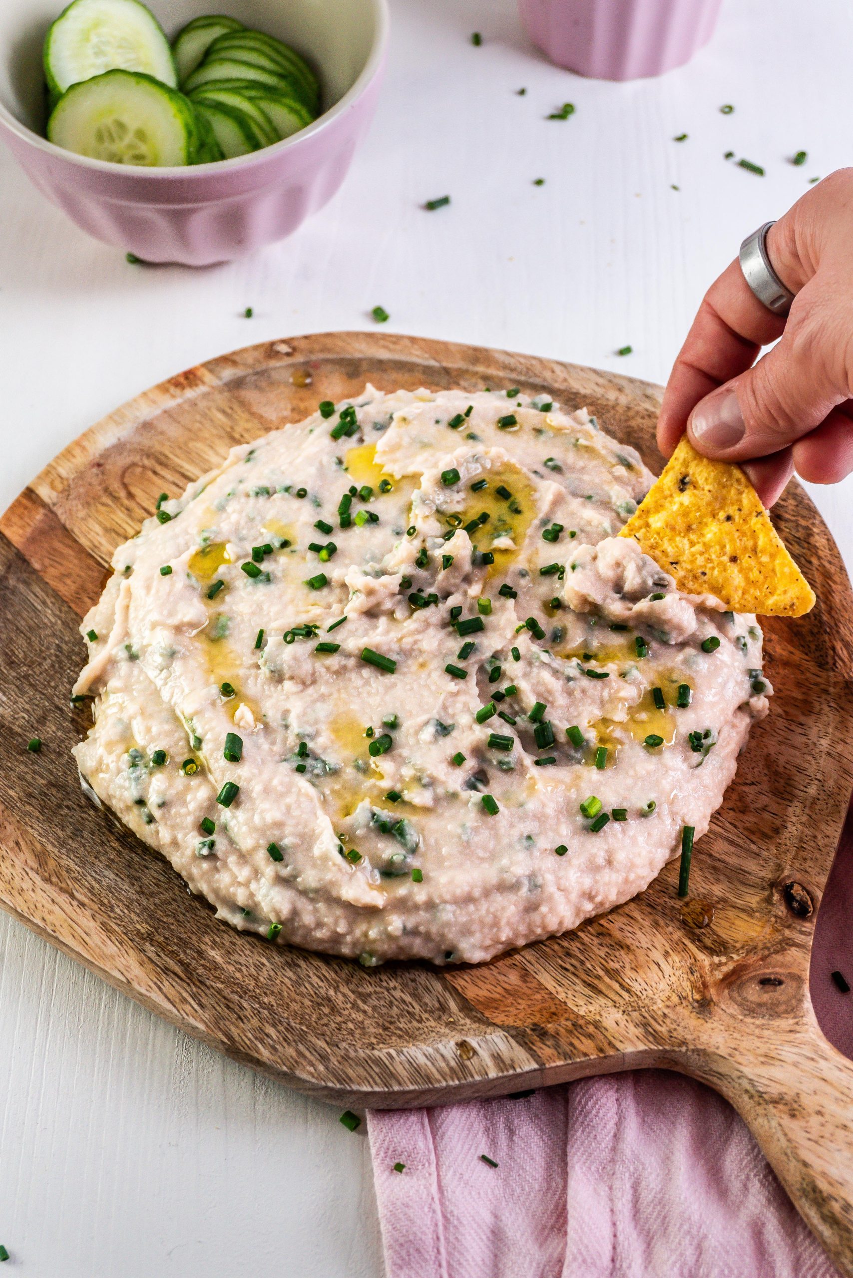 Quick and Easy Butterbean Dip on a wooden plate with a nacho being dipped into the dip