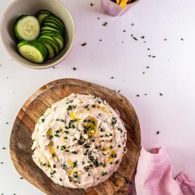 Quick and Easy Butterbean Dip on a wooden plate with cucumbers and nachos visible in the background and garnished with chives