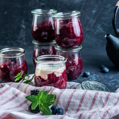 Red berry pudding ("Rote Grütze") in small glass jars with one having added some vanilla sauce on top
