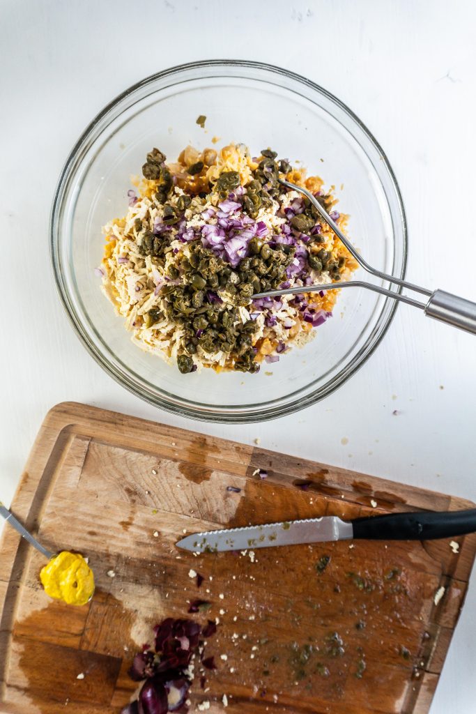 Mashed chickpeas, grated tofu, chopped capers and chopped red onion in a bowl for the vegetarian nicoise salad