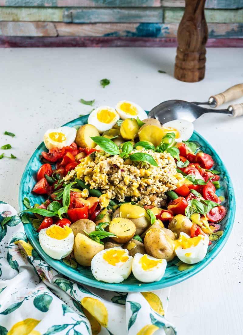 Vegetarian Nicoise Salad being served pretty on a plate with salad tongs visible in the background