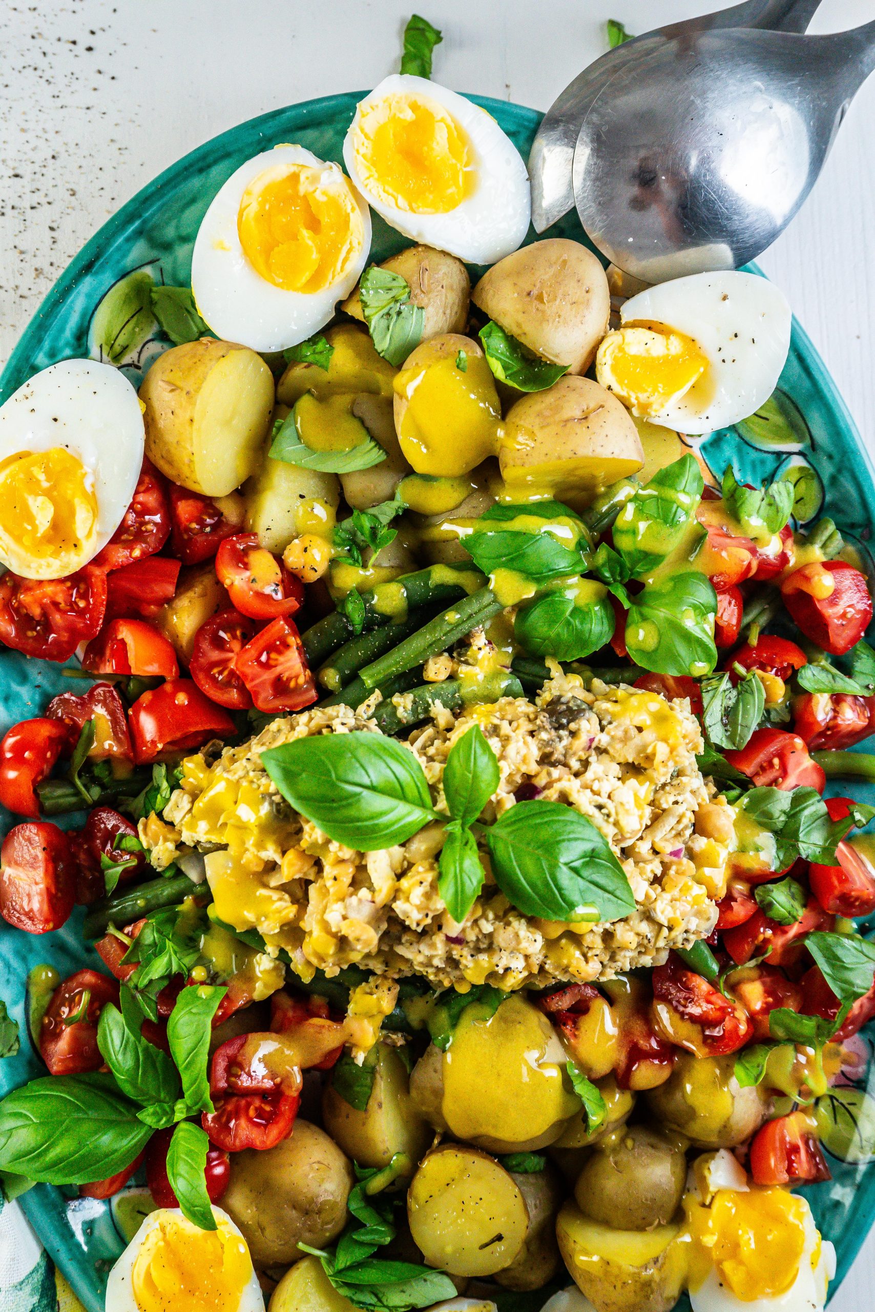 Vegetarian Nicoise Salad being served pretty on a plate with salad tongs visible in the background; photographed up close