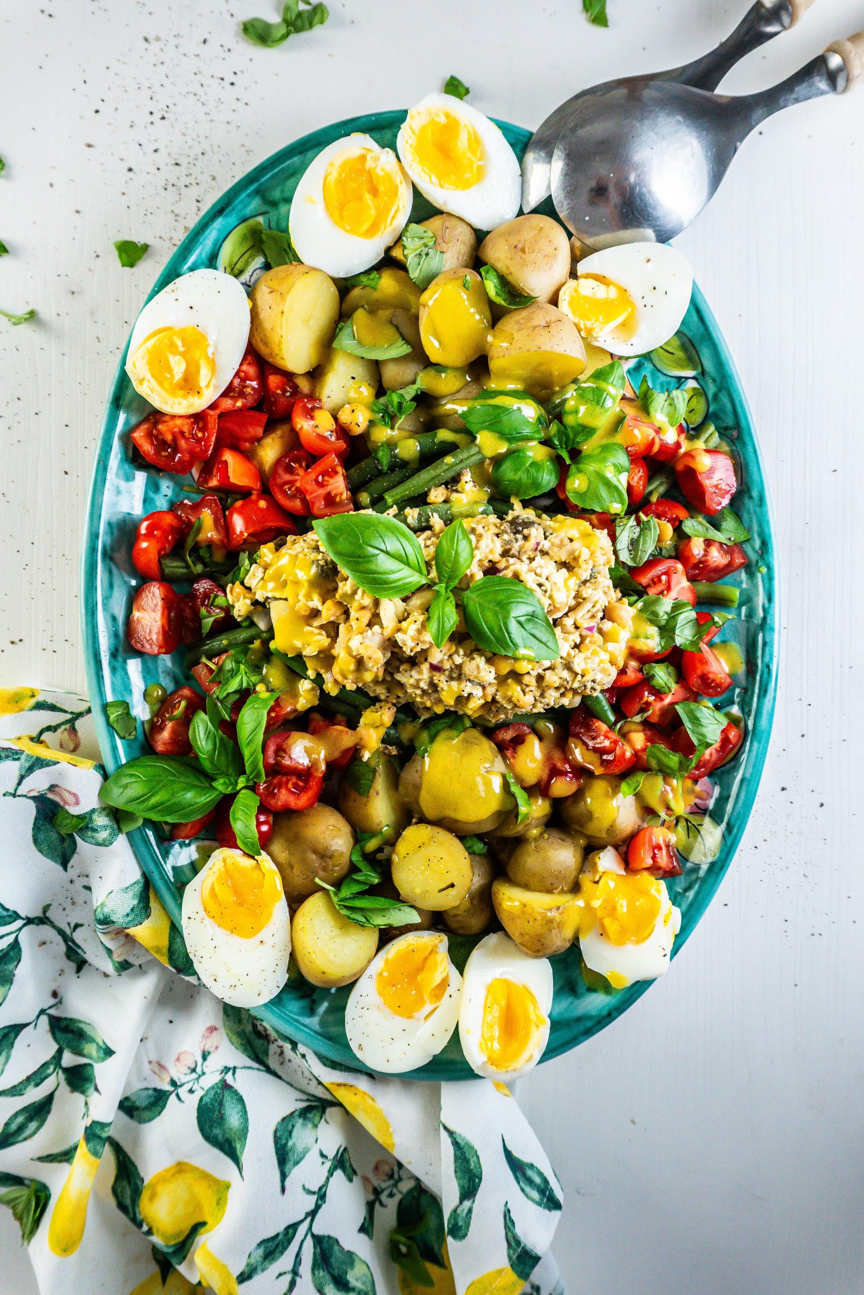 Vegetarian Nicoise Salad being served pretty on a plate with salad tongs visible in the background; photographed from above